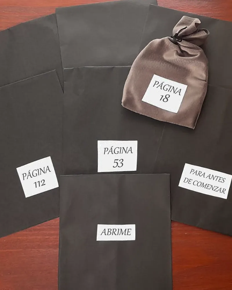 Sobres negros cerrados con etiquetas: «Página 18», «Página 53», «Página 112», «Abrime» y «Para antes de comenzar»